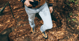 man in jeans carrying a camera through nature with leaf cover