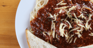 spaghetti and meat sauce on a white plate with bread