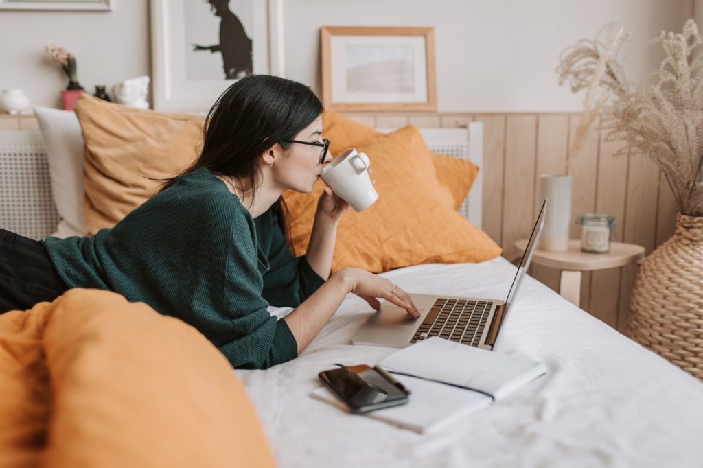 girl lying on bed drinking coffee at a computer