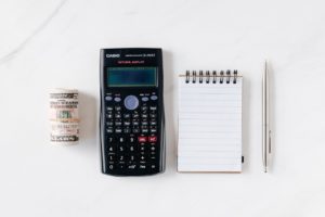 roll of money, calculator, notepad, and pen on white background