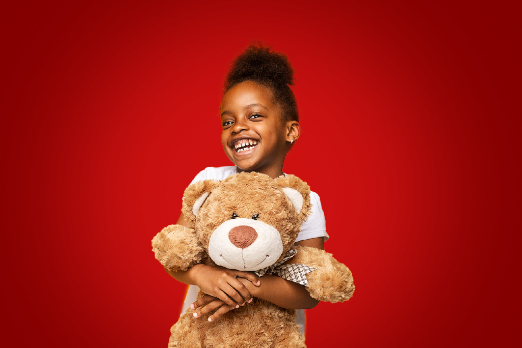 child hugging a big teddy bear on a red background