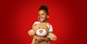 child hugging a big teddy bear on a red background