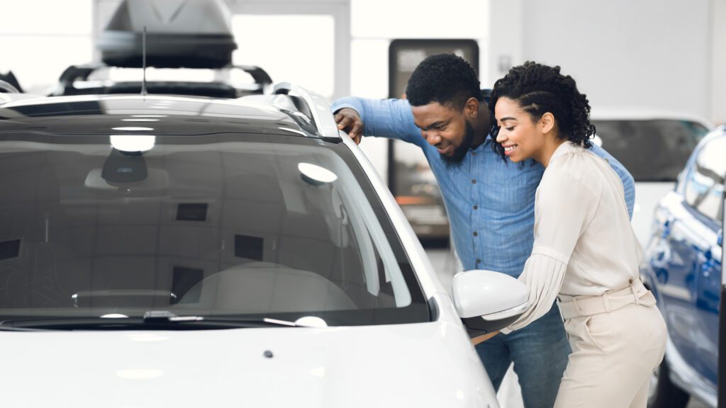 Couple Choosing Car Together Standing Near Vehicle In Showroom, Panorama