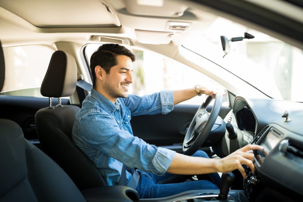 Handsome young man in denim shirt pressing touchscreen on car multimedia panel, switching shifting radio station.