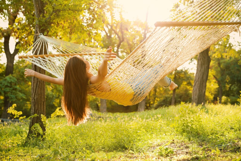 Young woman resting in comfortable hammock at green garden