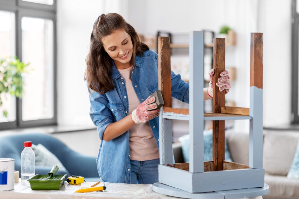 woman sanding old round wooden table with sponge